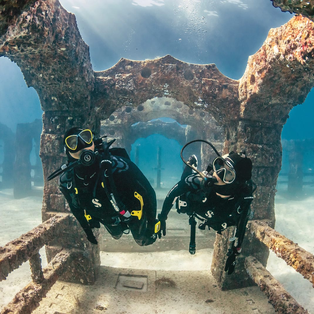 Two scuba divers explore underwater ruins